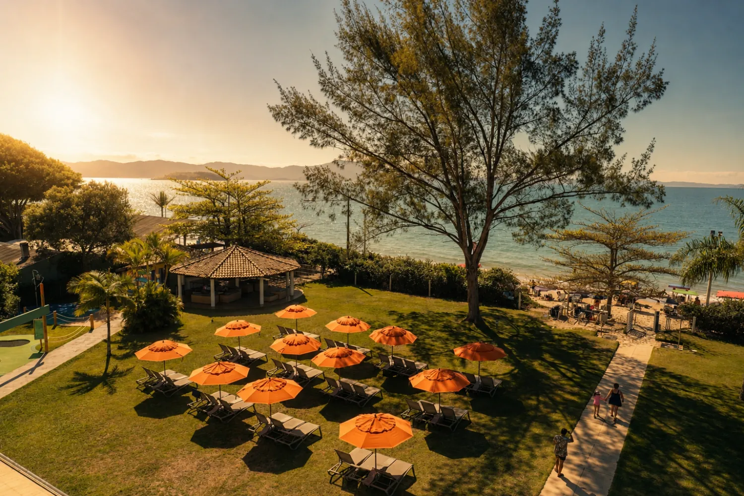Gramado do resort ao pôr do sol, com guarda-sóis laranja de frente para o mar