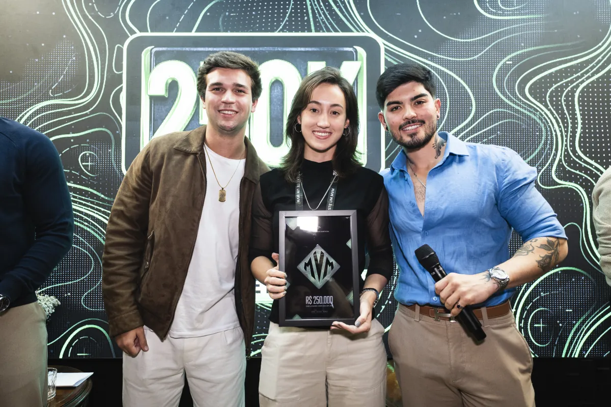 Três membros do MVM segurando a placa de faturamento conquistada